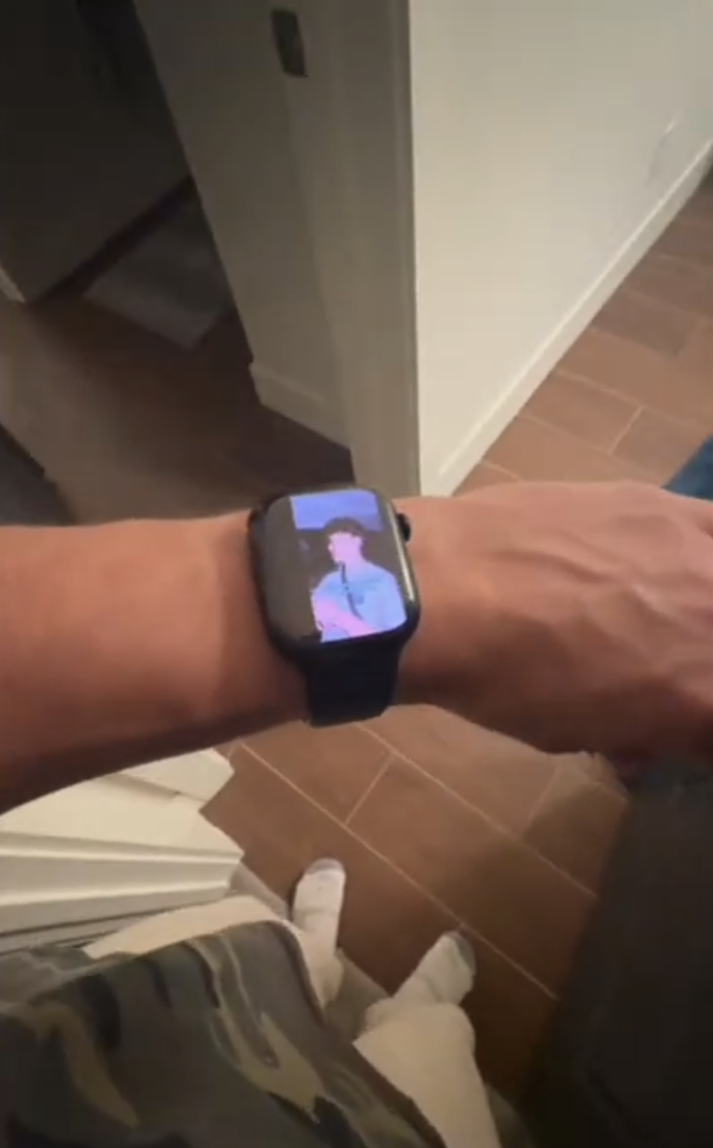 Apple Watch on a wrist playing a short-form vertical video while the wearer stands in a hallway