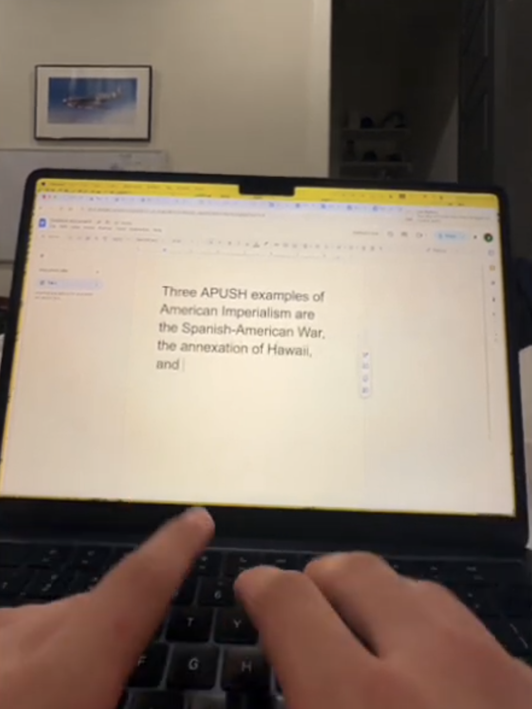 SentenceAI APUSH demo in Google Docs — laptop screen showing 'Three APUSH examples of American Imperialism are' followed by generated examples including the Spanish-American War and the annexation of Hawaii, while hands press random keys on the keyboard