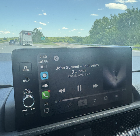 Photo from inside the family Honda CR-V on the highway up to Philly — dashboard screen on Apple CarPlay playing 'light years' by John Summit while a FedEx truck and green roadside trees pass outside the windshield